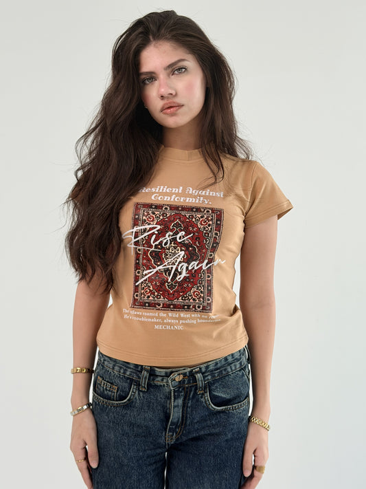 Woman wearing a tan t-shirt with graphic design and text on a plain background